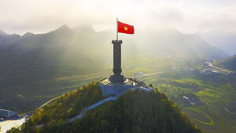 Cột cờ Lũng Cú với lá cờ đỏ sao vàng tung bay trên đỉnh núi Rồng, phía xa là phong cảnh núi non trùng điệp